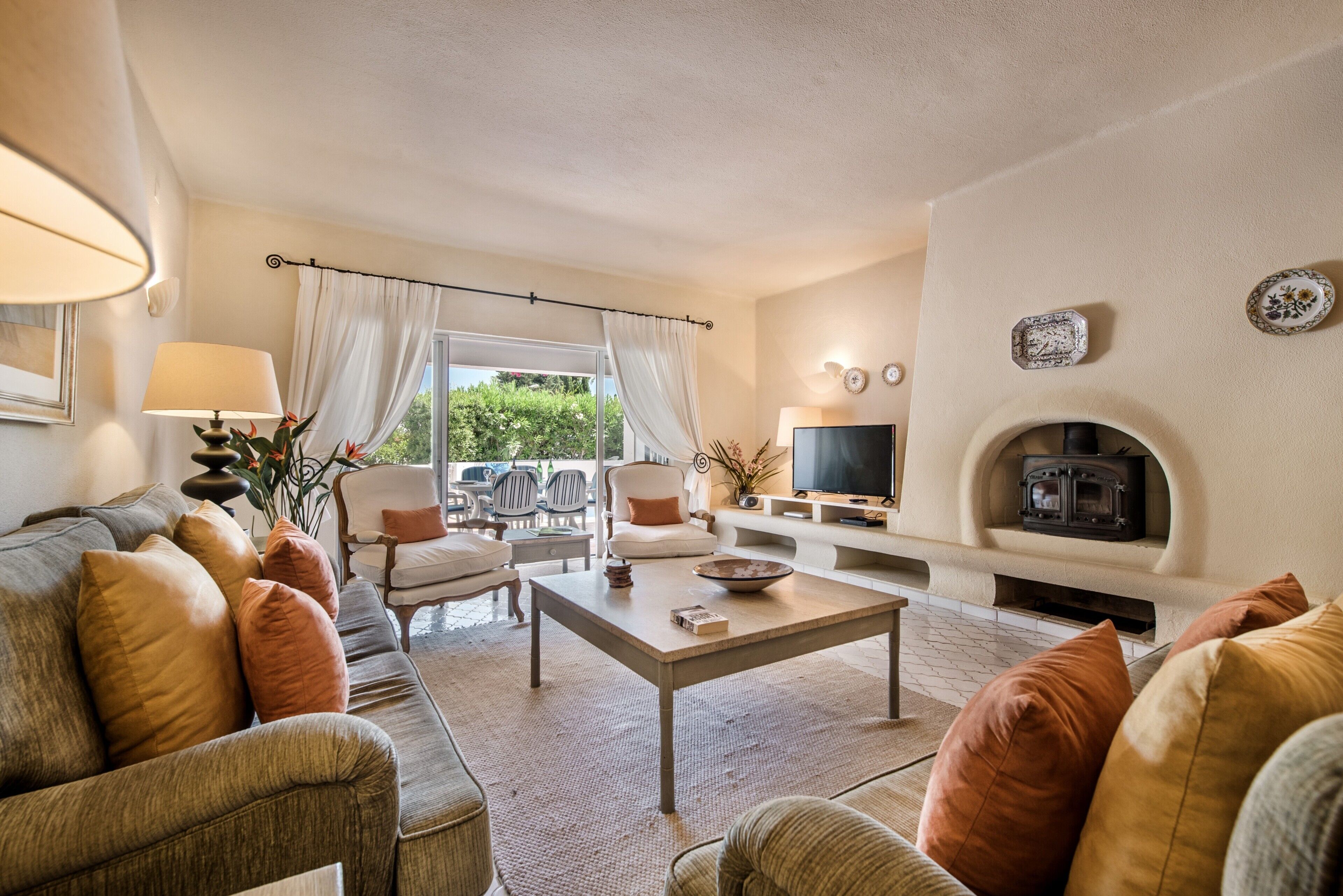 A living room with a sofa, chairs, a coffee table, a TV, a fireplace, and a view of greenery outside.