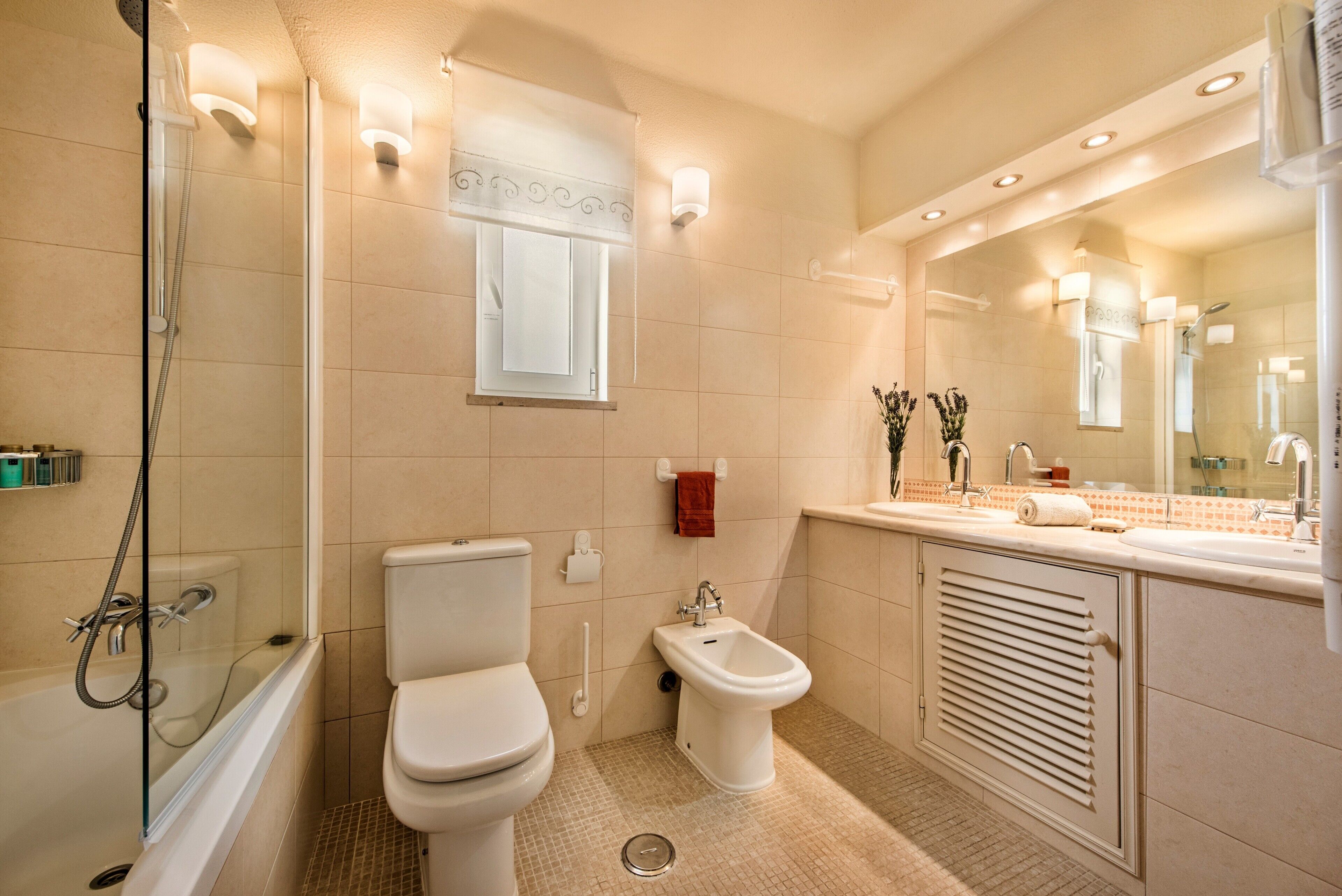 A modern bathroom with a shower, toilet, bidet, and a large mirror.