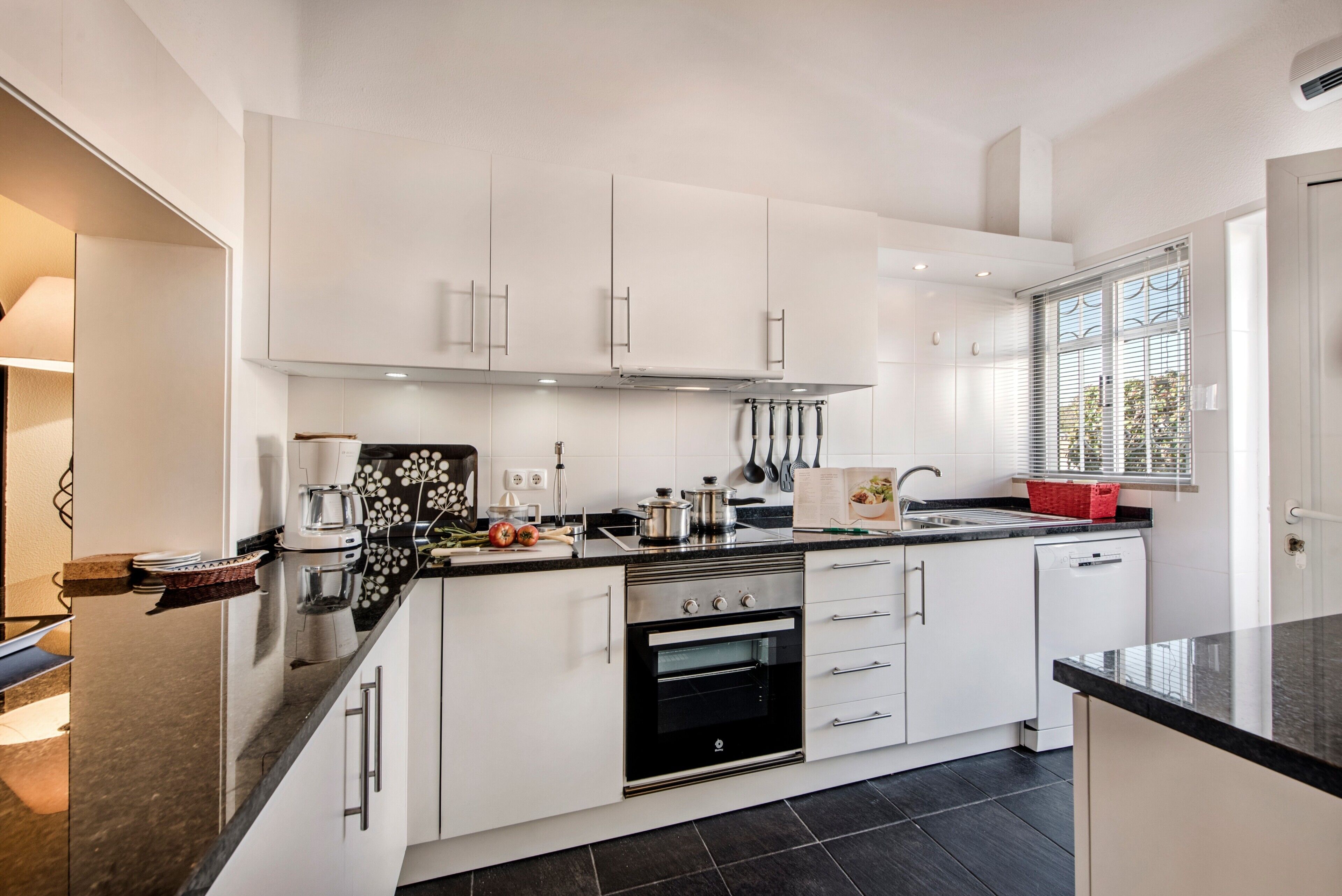 A modern kitchen with white cabinetry, a black oven, and a window with blinds.