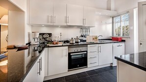 A modern kitchen with white cabinetry, a black oven, and a window with blinds. - Villa "Mng Elliott 74" with Private Pool and Wi-Fi (Vale do Lobo)