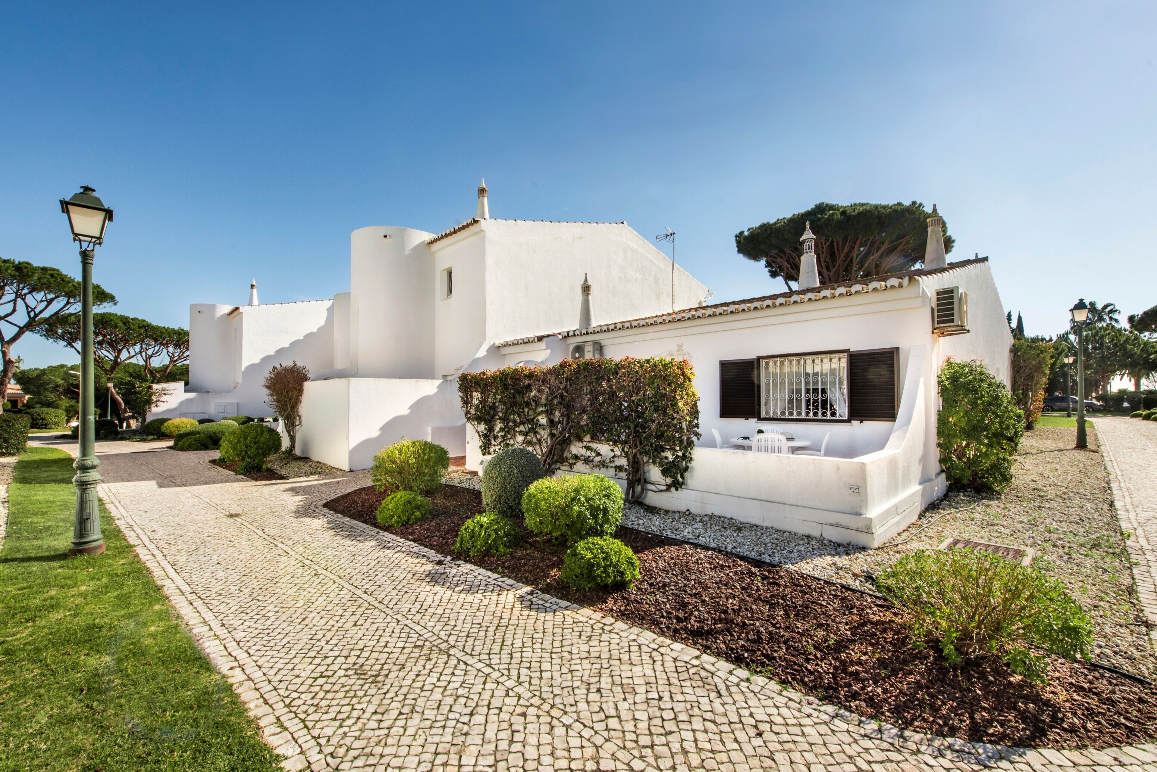 A white building with a paved pathway, trimmed hedges, and a small garden area.