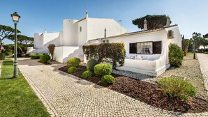 A white building with a paved pathway, trimmed hedges, and a small garden area. - Villa "Mng Elliott 74" with Private Pool and Wi-Fi (Vale do Lobo)