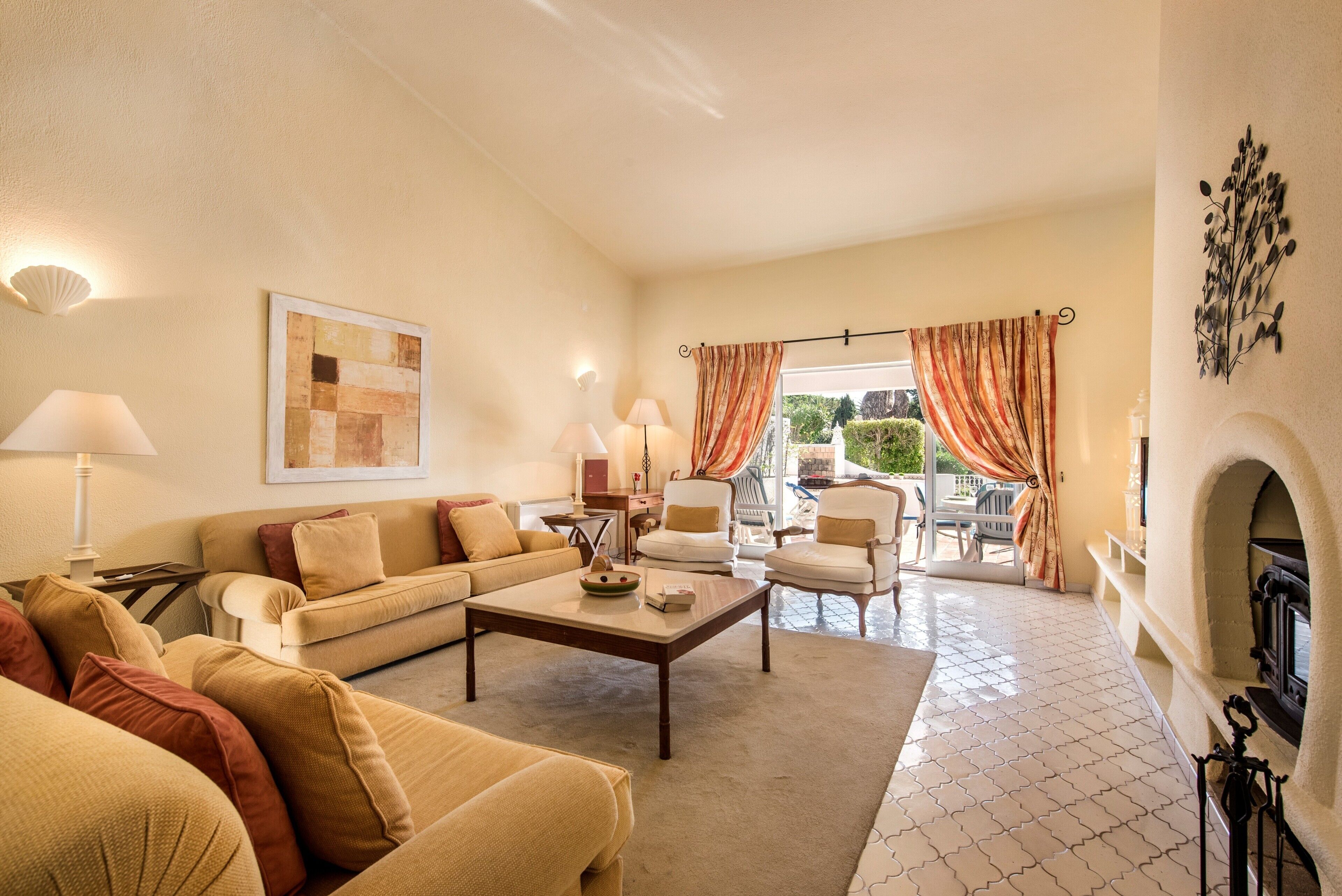 A living room with a sofa, armchairs, a coffee table, a fireplace, and a view through a glass door.