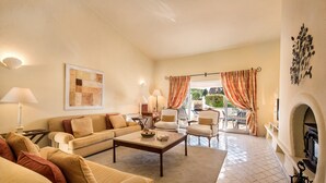 A living room with a sofa, armchairs, a coffee table, a fireplace, and a view through a glass door. - Villa "Mng Elliott 74" with Private Pool and Wi-Fi (Vale do Lobo)