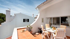 A terrace with a table set for dining, chairs, a potted plant, and a window overlooking the surroundings.