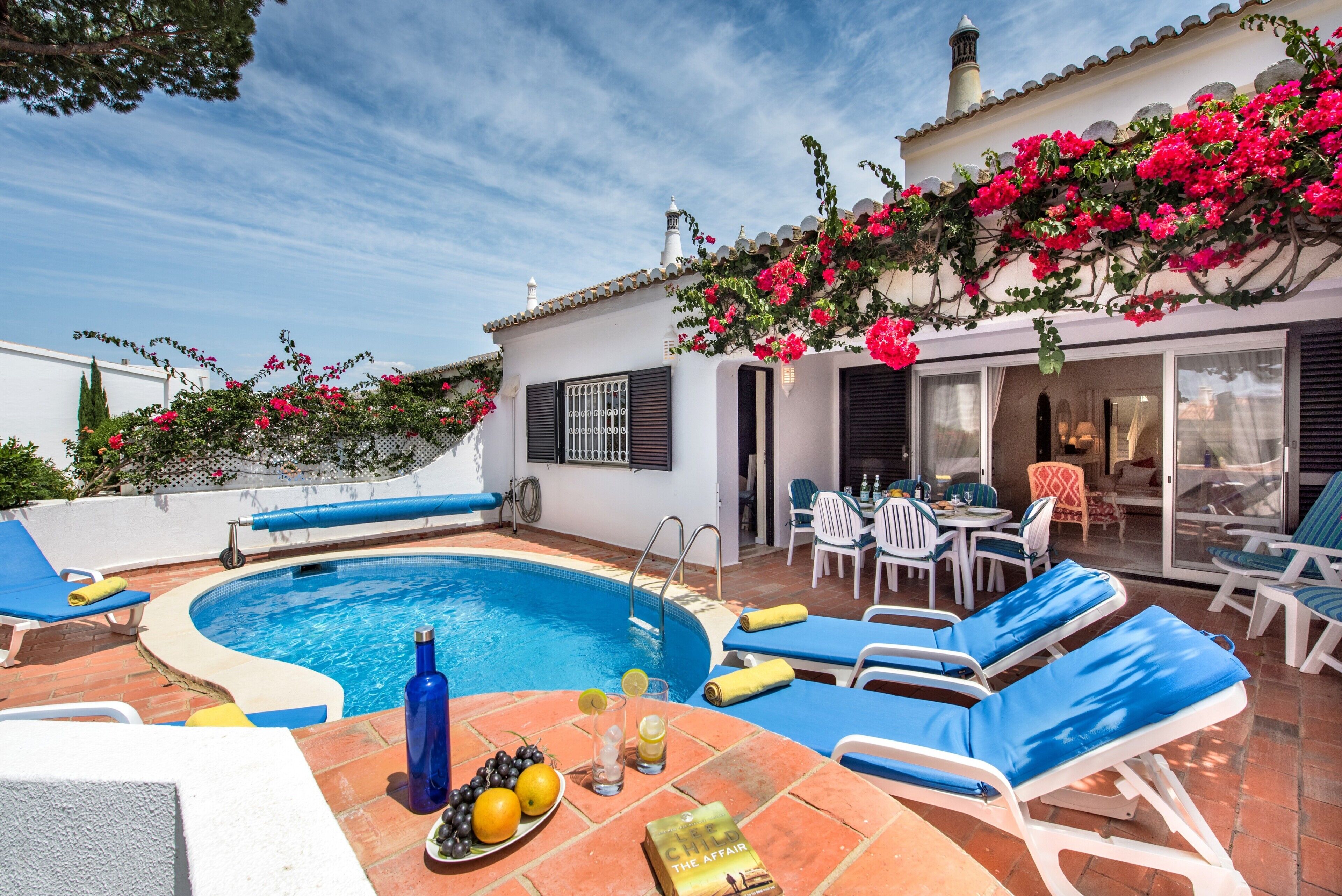 A pool area with lounge chairs, a table with drinks, and a book titled 'The Affair'.