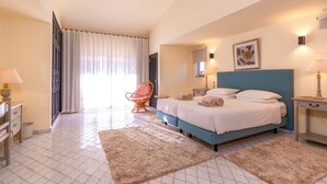 Ein Schlafzimmer mit einem Bett, einem Sessel, einem Nachttisch, einer Lampe und einem Fenster mit Vorhängen.