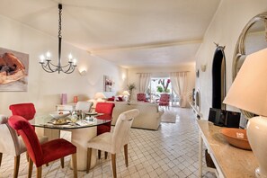 A modern living room with a glass dining table, red chairs, a white sofa, and a chandelier.