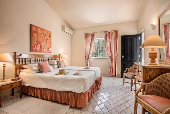 Une chambre avec deux lits, une tête de lit en bois, une table de chevet avec une lampe, une chaise, une commode et une fenêtre avec des rideaux.