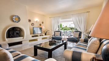 Un salon avec une cheminée, un canapé, des fauteuils et un téléviseur.