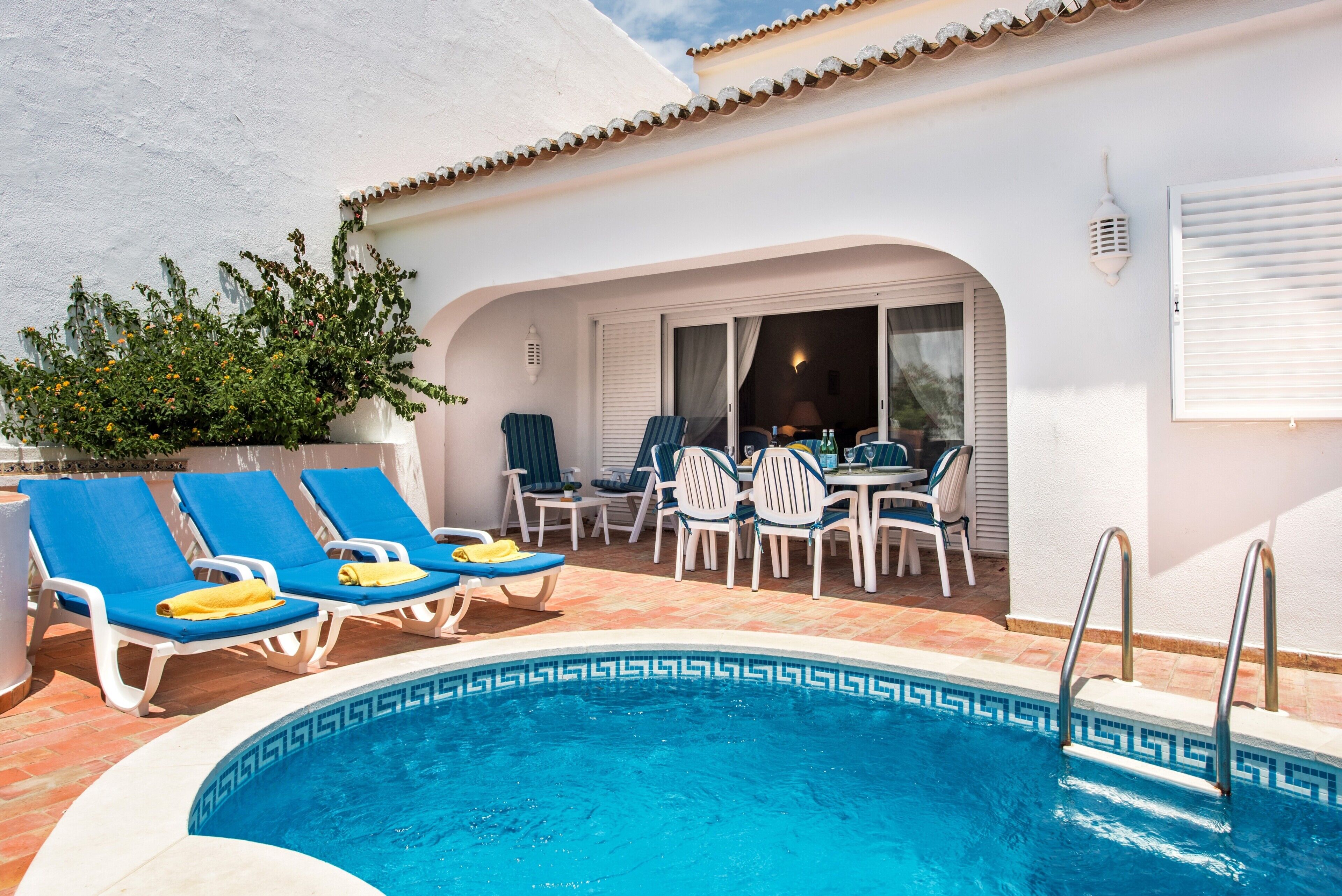 Un espace piscine aménagé avec des chaises longues, une table et des chaises.