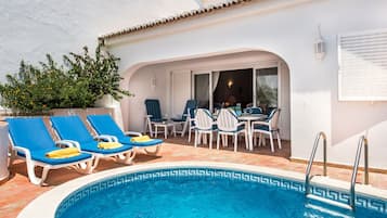 Un espace piscine aménagé avec des chaises longues, une table et des chaises.