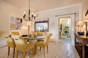 Un coin repas avec une table ronde, quatre chaises, un lustre et une cuisine visible à travers un miroir.