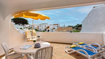 Un balcon avec des chaises blanches, une table et un parasol jaune.