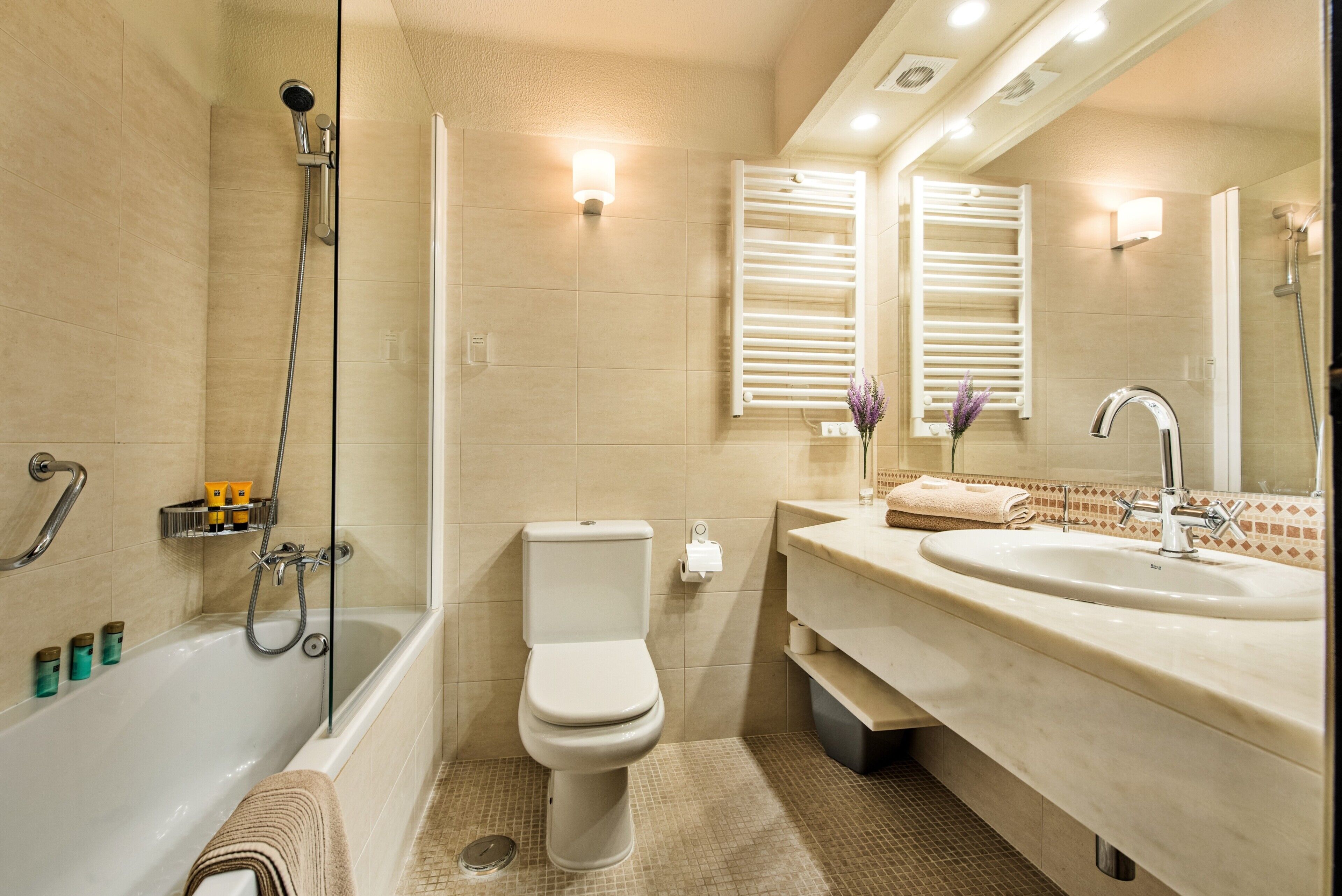 Ein modernes Badezimmer mit Badewanne, Toilette und Waschbecken, ausgestattet mit Handtuchhalter und Spiegel.