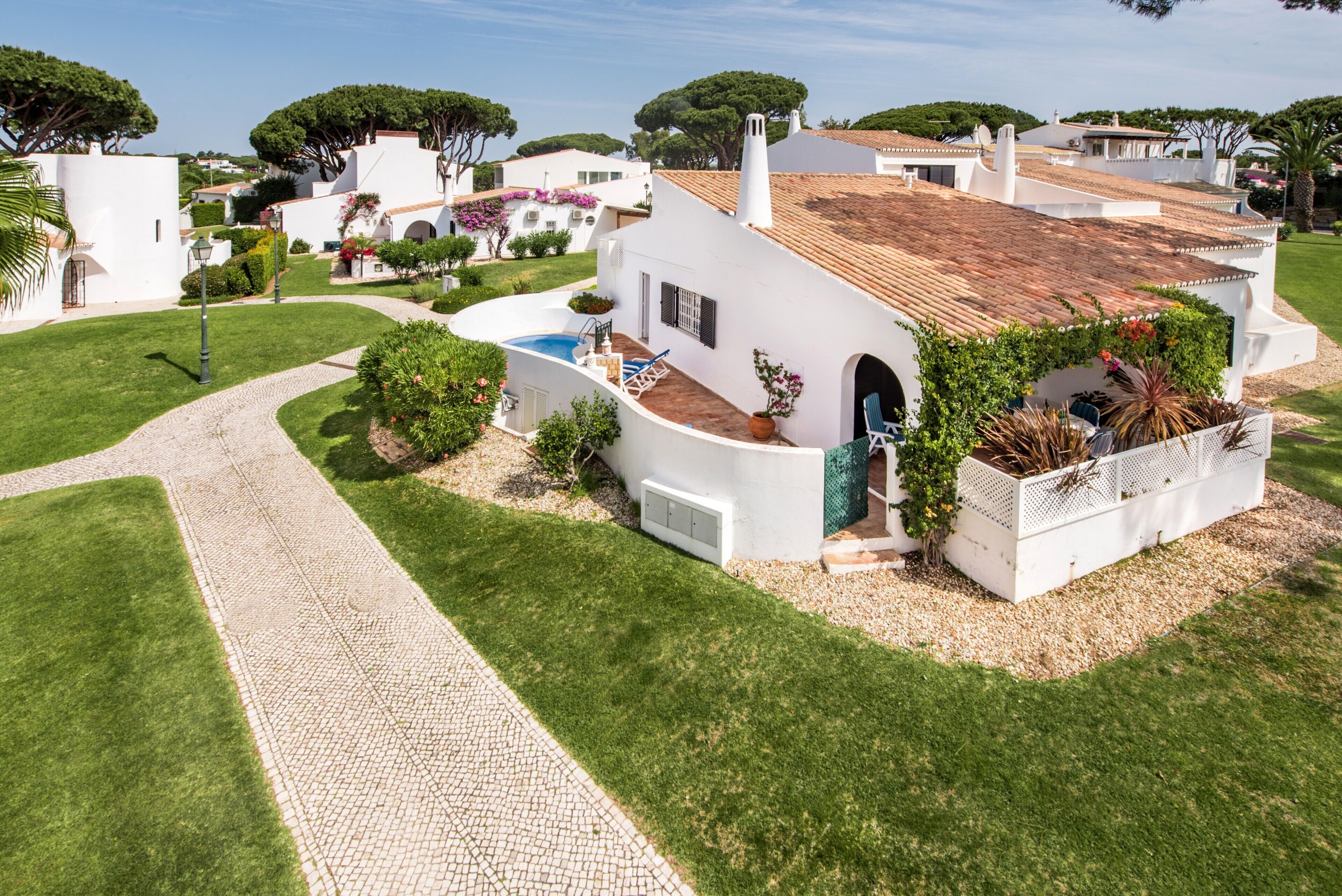 A white villa with a tiled roof, a paved driveway, and a small pool.
