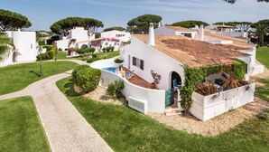 Una villa blanca con techo de tejas, un camino de entrada pavimentado y una piscina pequeña.