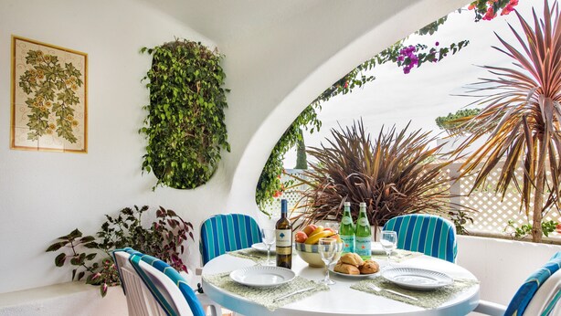 Una mesa redonda con sillas a rayas azules, una pared blanca con un cuadro de hojas verdes y un techo blanco con un diseño curvo.