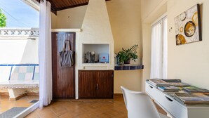 Ein Zimmer mit Fliesenboden, einer Holztür, einem weißen Schreibtisch mit Büchern, einer Topfpflanze und einem an der Wand hängenden Kunstwerk.