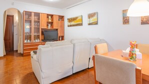 Ein Wohnzimmer mit Sofa, Fernseher, Holzschrank und Esstisch.