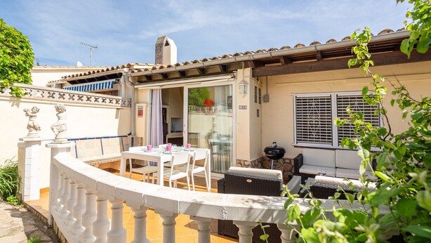 Eine Terrasse mit Tisch, Stühlen, einem Grill und einer Glastür zu einem Innenbereich.