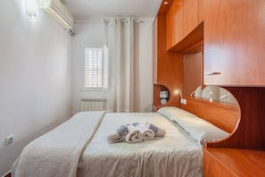 Una habitación de hotel con cama, un espejo redondo, una ventana con cortinas y un equipo de aire acondicionado.