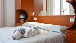 Ein ordentlich gemachtes Bett mit Handtüchern, einer Nachttischlampe und einem Nachttisch aus Holz mit Lampe.