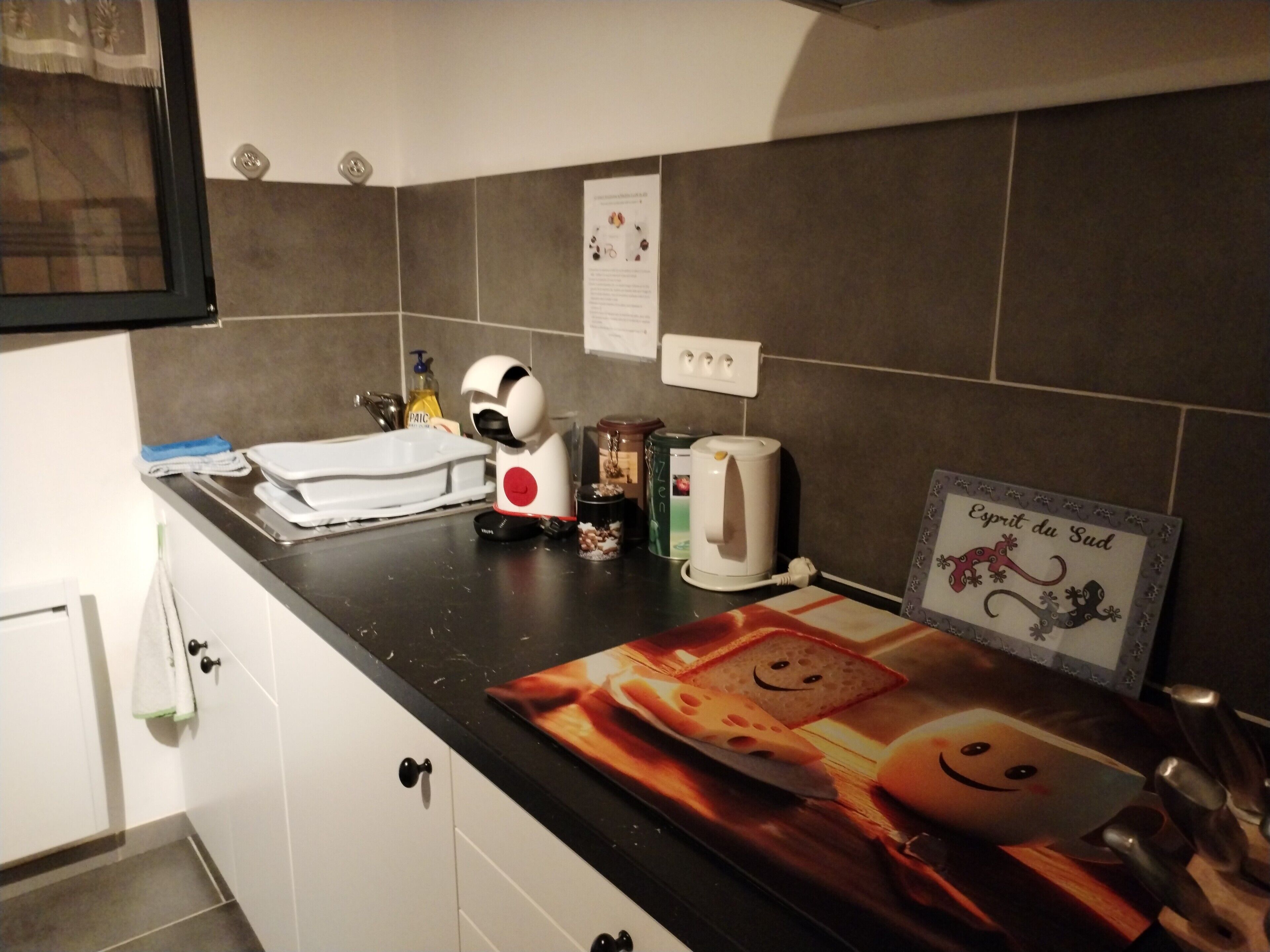 Eine Küche mit schwarzem Arbeitsplatz, einem Wasserkocher, einer Kaffeemaschine und einem gerahmten Bild an der Wand.