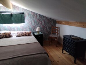 Ein Schlafzimmer mit einem Bett, einem Sessel, einer Kommode und einem Nachttisch mit Lampe.