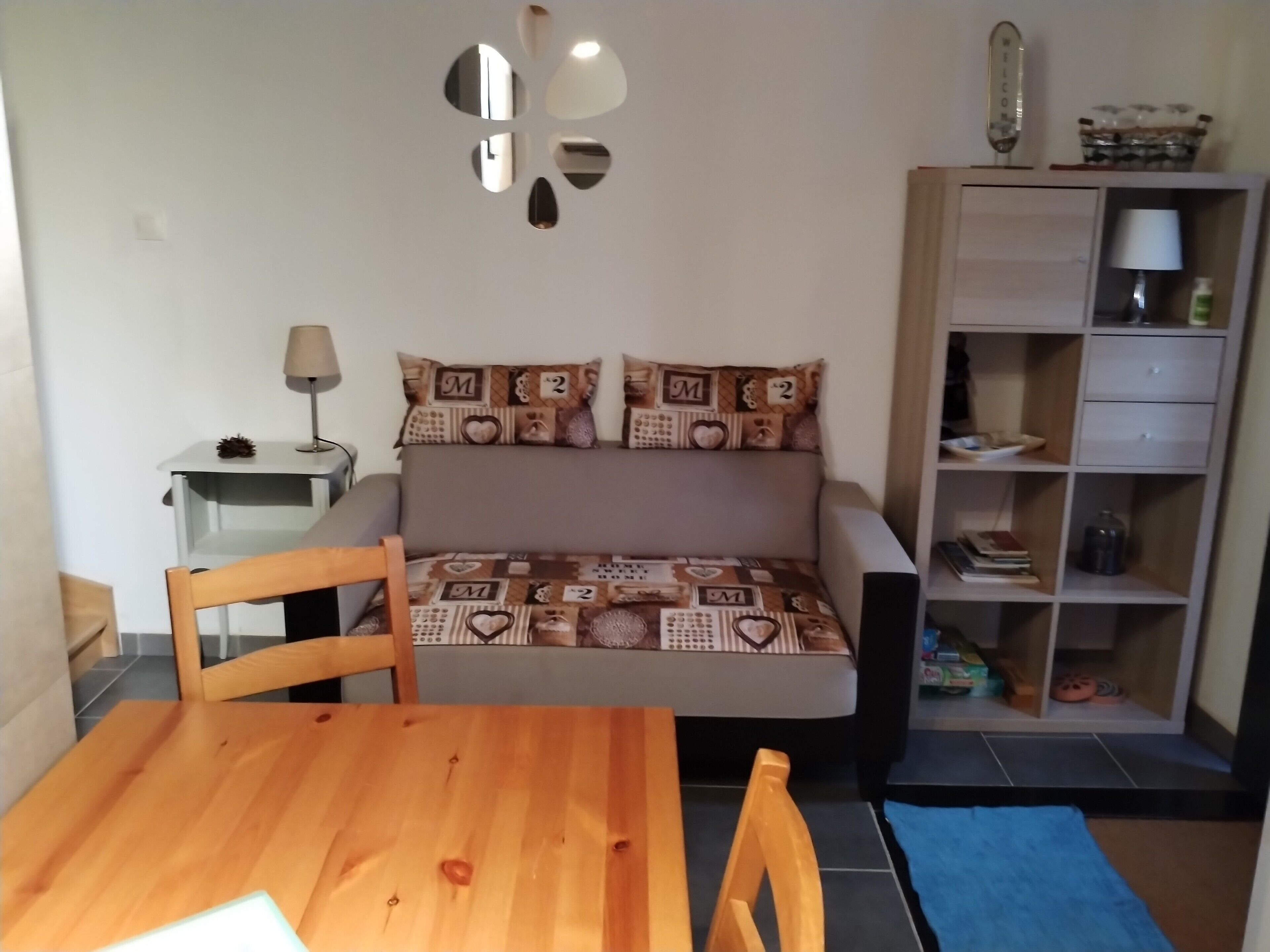 Een kamer met een bed, een houten tafel, een lamp, een boekenplank en een spiegel aan de muur.