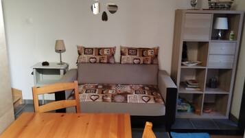 Een kamer met een bed, een houten tafel, een lamp, een boekenplank en een spiegel aan de muur.