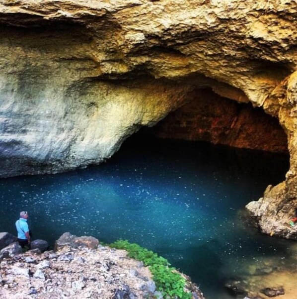 Une grotte avec une mare, des parois rocheuses et une personne debout sur une corniche.