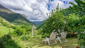 Un jardín con dos sillas blancas, una rosa roja y vistas de un valle con montañas.