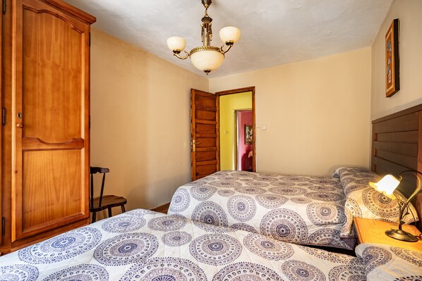 Un dormitorio con un armario de madera, una cama con ropa de cama estampada, una mesita de noche con lámpara y un candelabro.