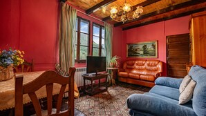 Una habitación con techo de madera, pared roja, sofá de cuero marrón, sofá azul, televisor sobre un mueble de madera y una mesa de comedor con sillas.