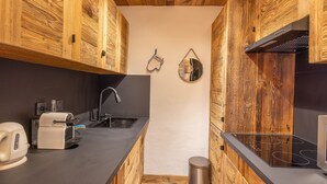 A kitchen with wooden cabinets, a black countertop, a coffee machine, a sink, and a stove.