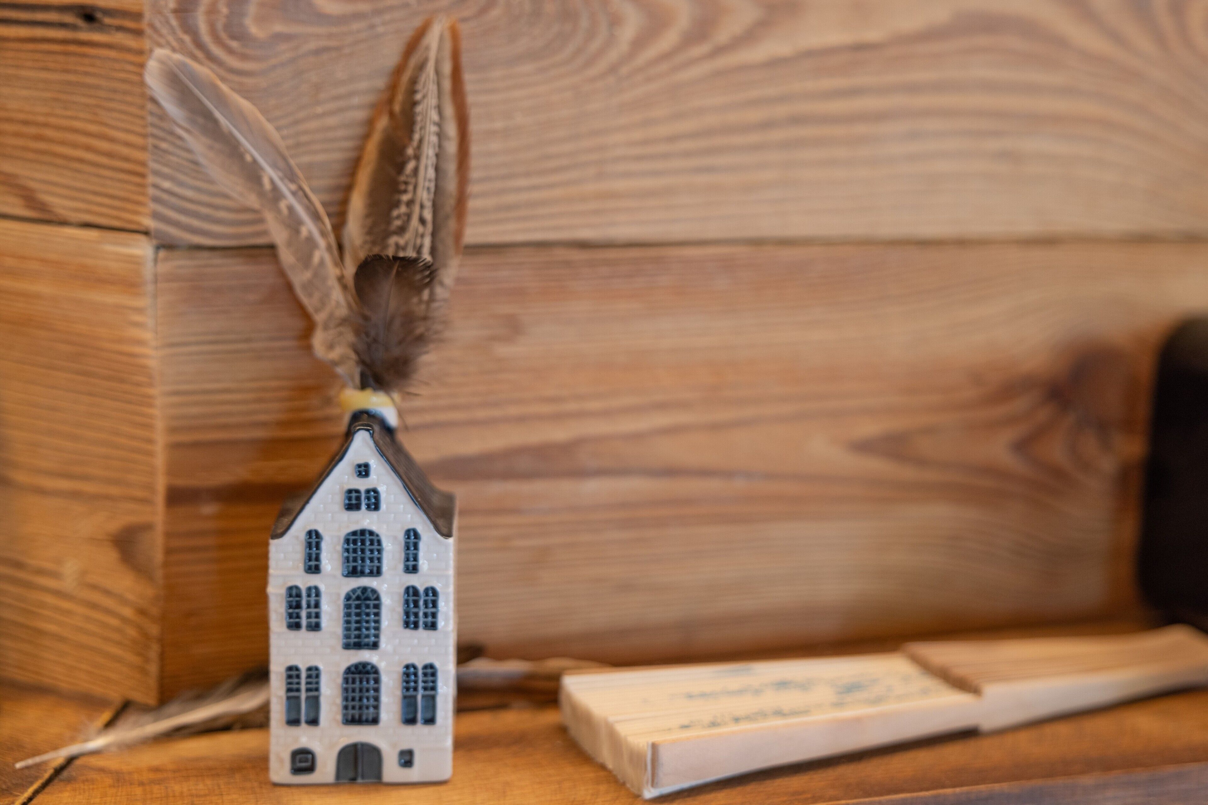 Een modelhuis met een veertje bovenop, op een houten ondergrond.