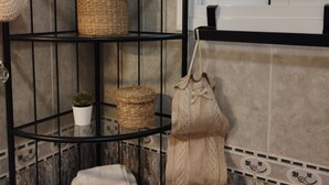 Une salle de bain avec une étagère en métal noir où sont posés des paniers, un pot de fleurs, une serviette et un sac suspendu.