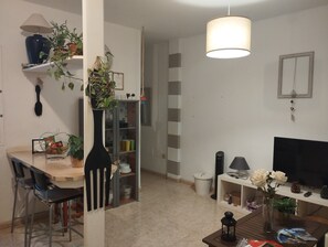 Olohuone, jossa on televisio, sohvapöytä, kirjahylly ja ruokailutila tuoleineen.