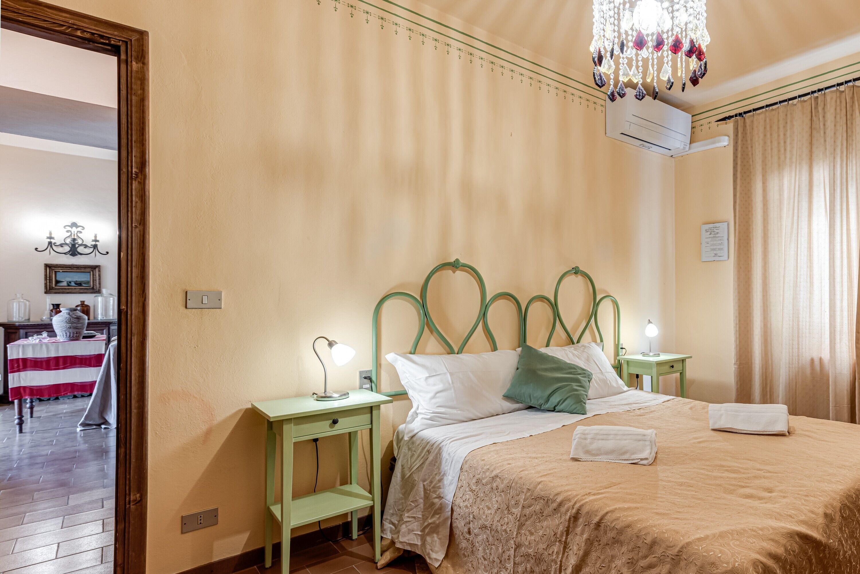 Ein Zimmer mit einem Bett, einem Nachttisch, einem Tisch mit Tischdecke und einer Chandelüster.