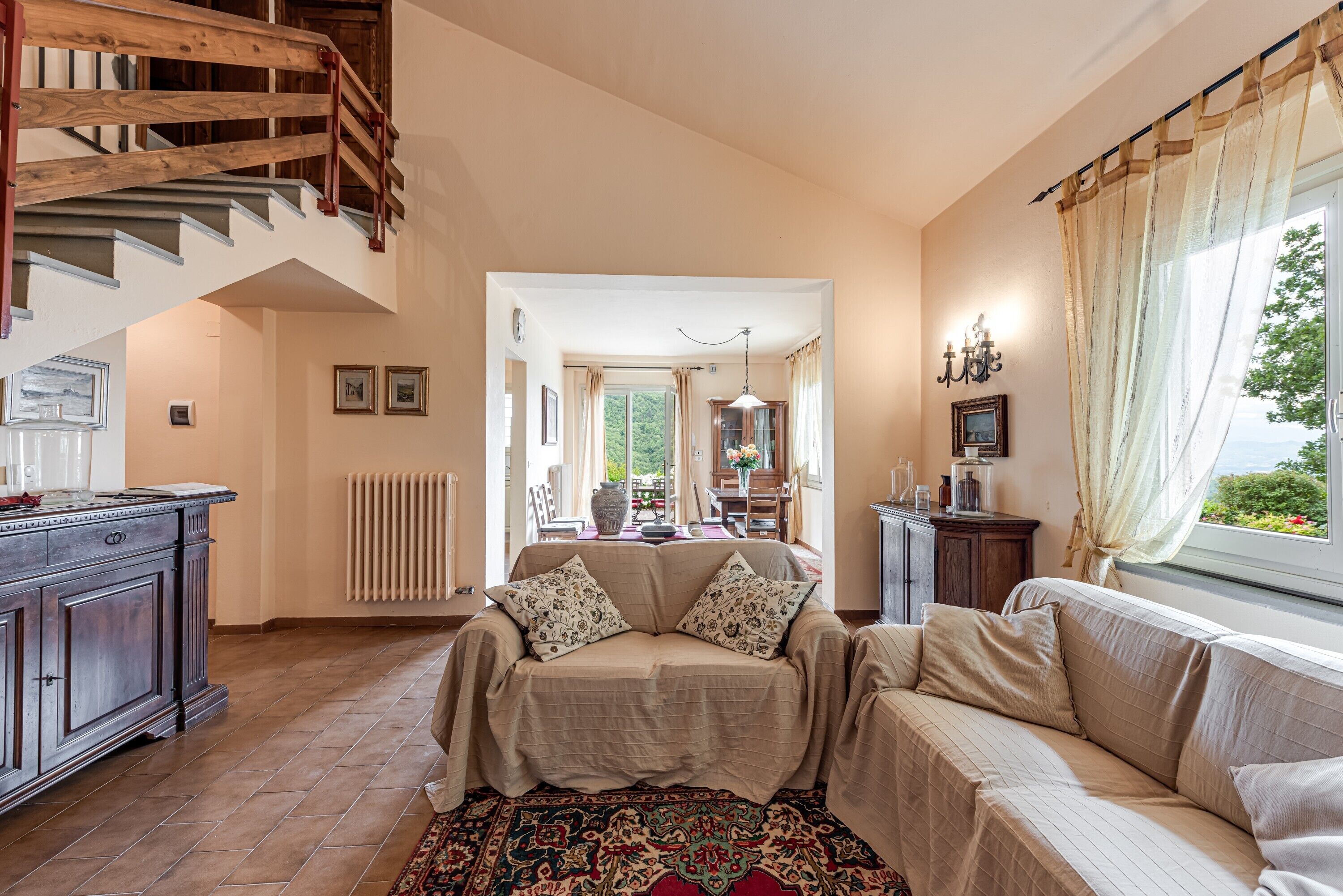 Un amplio espacio habitable con una escalera, un conjunto de sofás, un comedor y vistas por una ventana.