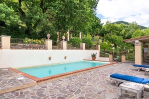 Una piscina con suelo de piedra, rodeada por un muro blanco y una valla de metal.