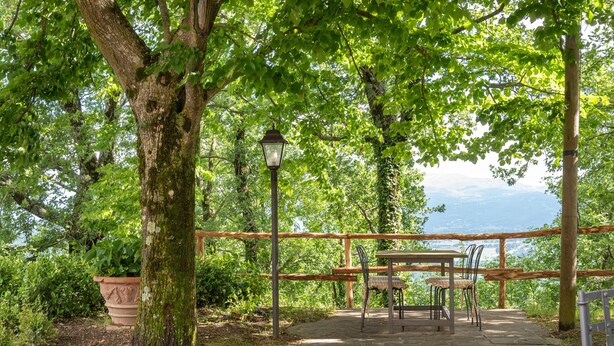 Ein Steinweg führt zu einer Holzbank mit Tisch und Stühlen, umgeben von Bäumen und Blick auf die Landschaft.