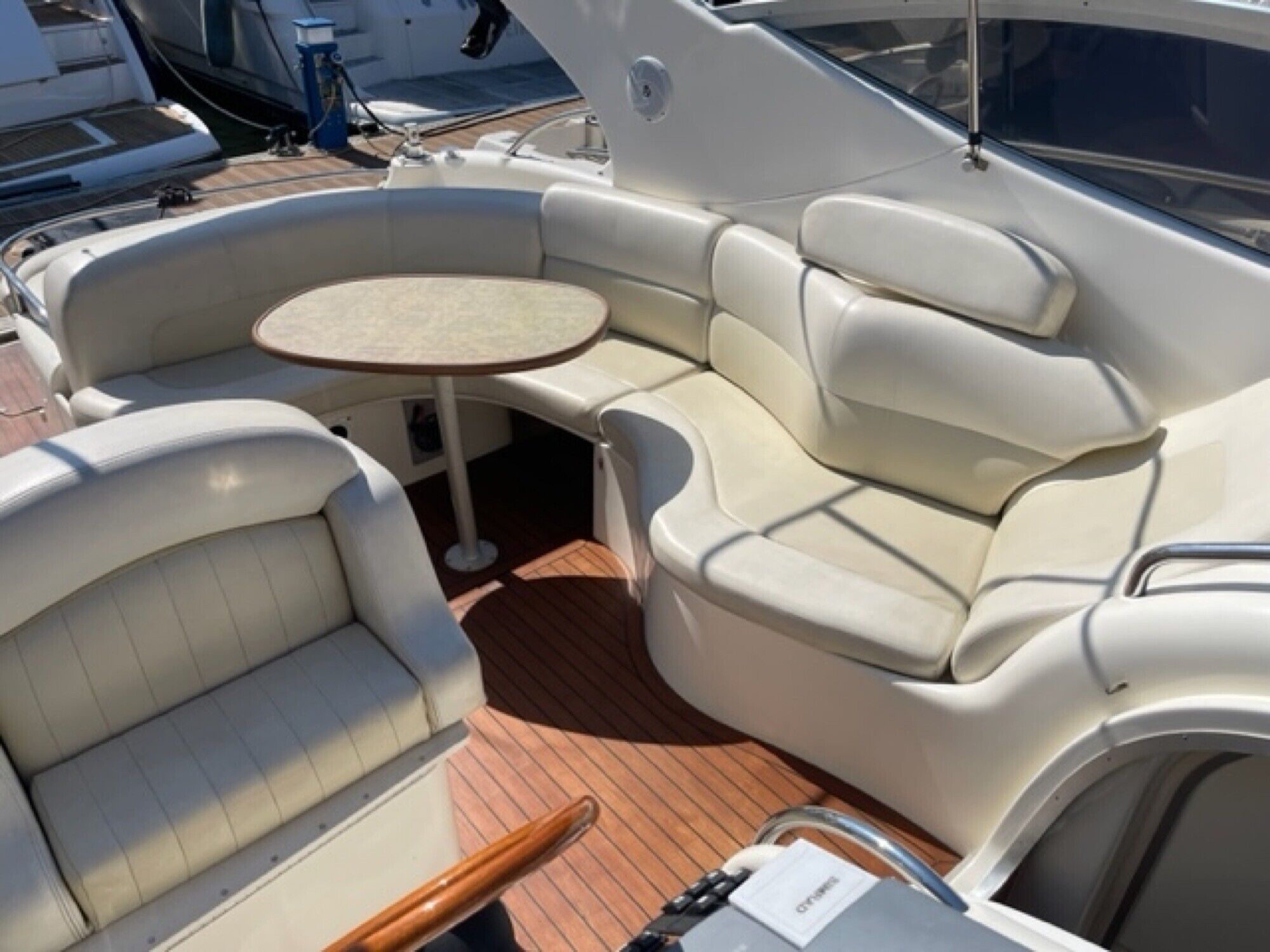 Interior de un barco con zona de asientos acolchada, una mesita y un timón.