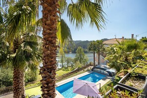 A swimming pool with a view of a lake, surrounded by palm trees and a fenced deck area. - Holiday Home 'Porto Douro' with Private and Indoor Pools, Heated Water, Terrace and Wi-Fi (Foz do Sousa)
