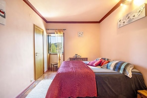 Ein Schlafzimmer mit einem Bett, einem Nachttisch, einem Fenster mit Vorhängen, einer Tür und einem kleinen Tisch.