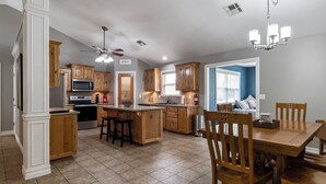 A modern kitchen with wooden cabinets, a central island, and a dining area with wooden chairs. - Lakeview Home in serene setting, 3 mi to Grove! Perfect for families & fishermen (Grove)