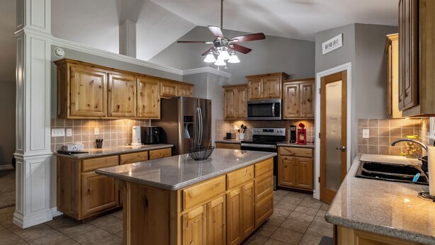 A kitchen with wooden cabinets, a stainless steel refrigerator, a microwave, and a large island with a sink. - Lakeview Home in serene setting, 3 mi to Grove! Perfect for families & fishermen (Grove)