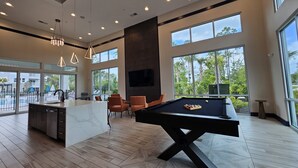 A spacious room with a pool table, comfortable seating, and large windows offering a view of the outdoors.