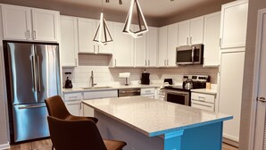 A modern kitchen with white cabinets, stainless steel appliances, and a blue accent wall.